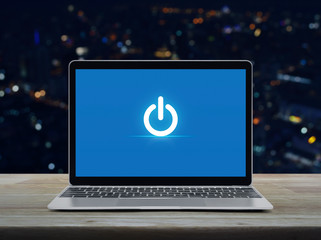 Power button icon on modern laptop computer on wooden table over blur colorful night light office city tower and skyscraper, Start up business online concept