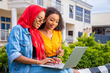 Beautiful African Women Sitting Outside In A Park Together Enjoying Shopping Online Together