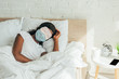© LIGHTFIELD STUDIOS - african american woman in sleep mask and medical mask sleeping on white bedding