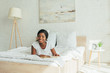 © LIGHTFIELD STUDIOS - cheerful african american girl lying on bed with book and smiling at camera