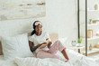 © LIGHTFIELD STUDIOS - smiling african american girl with sleep mask on forehead sitting in bed, holding book and looking at camera