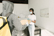 © LIGHTFIELD STUDIOS - back view of courier giving pizza boxes to african american girl in medical mask