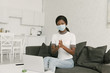 © LIGHTFIELD STUDIOS - young african american freelancer in medical mask disinfecting hands while sitting near laptop in kitchen