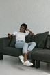 © LIGHTFIELD STUDIOS - pretty african american girl holding tv remote controller while sitting on sofa at home