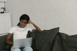 © LIGHTFIELD STUDIOS - smiling african american freelancer sitting on sofa and using laptop