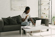 © LIGHTFIELD STUDIOS - pretty african american girl using laptop and holding credit card while sitting on sofa at home