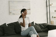 © LIGHTFIELD STUDIOS - cheerful african american girl sitting on sofa, talking on smartphone and looking away