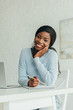 © LIGHTFIELD STUDIOS - happy african american freelancer smiling at camera while holding pencil near notebook and laptop