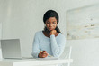 © LIGHTFIELD STUDIOS - attentive african american freelancer writing in notebook while sitting near laptop
