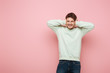 shocked man covering ears with hands while grimacing with closed eyes on pink background