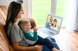 © Vadim Pastuh - Little grandson is talking via video call on laptop with a grandparents. A young mother with a baby son sit on a sofa at home and have a video meeting grandparent are on a laptop screen