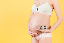 Close Up Image Of Thirty Weeks Of Pregnancy Cubes In Pregnant Woman's Hands At Yellow Background. Happy Pregnancy. Copy Space