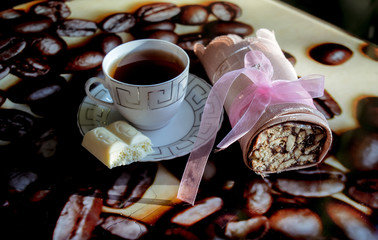 a sweet roll wrapped in cloth lies by a cup of tea on a saucer which contains two pieces of white chocolate