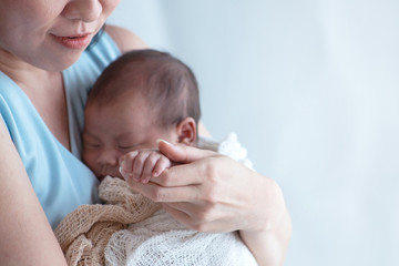 Asian mother is holding newborn baby in her arms. her hands hold the baby's hands, happy mother and baby enjoy spending time together