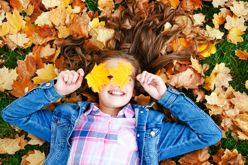 Autumn portrait of adorable smiling little girl child preteen lying in leaves in the park