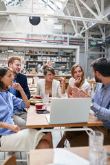 young man showing and explaining content on laptop to colleagues in restaurant at lunchtime