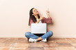 © luismolinero - Young mixed race woman with a laptop sitting on the floor pointing with the index finger a great idea