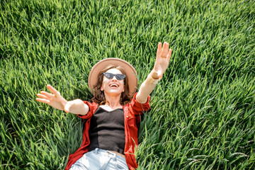 Portrait of a stylish carefree woman lying on the greenfield enjoying nature in springtime, view from above. Concept of wellness and carefree lifestyle on nature