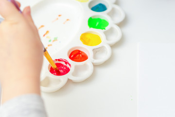 Wall Mural - Closeup of child's hand holding brush over watercolors palette on white sheet of paper. The child is ready to paint with watercolors.