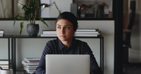 Canvas Print - Serious young indian businesswoman student or worker using laptop computer tech working from home. Ethnic professional female employee thinking searching ideas looking away doing online job in office.