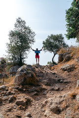 Wall Mural - Man Tourism traveler hiker with a backpack standing on the rock hands up enjoi nature with olive trees, travel Hiking adventure lifestyle holiday vacation healthy concept. Vertical photo