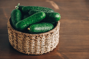 Fresh green cucumbers in a wicker basket on a wooden table background. Copy, empty space for text