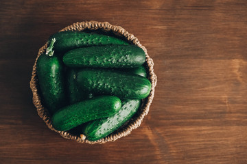 Fresh green cucumbers in a wicker basket on a wooden table background. Top view. Copy, empty space for text