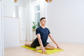 Wall Mural - Resolved, detemined young man doing yoga on a mat at home, lifting upper body