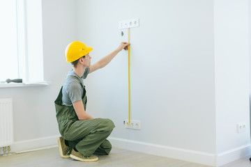 the builder in the helmet takes measurements on the wall, finishing work in apartments, repairing the house.