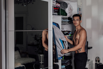 a guy without a shirt chooses clothes near the closet