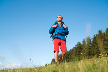Wall Mural - middle-aged backpacker traveler looking at sunset and preparing for trekking at summertime sunny day