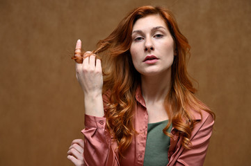 Photo portrait on a beige background of a pretty young woman in a pink shirt with long beautiful red hair. The model shows sad emotions.