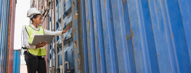 Black foreman woman worker working checking at Container cargo harbor holding laptop computer to loading containers. African dock female staff business Logistics import export shipping concept.