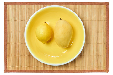 Wall Mural - bright lemon and pale mango on a yellow plate on a cane tablecloth