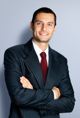 Wall Mural - Portrait of cheerful confident businessman in white shirt and red tie, crossed arms pose, standing against grey background