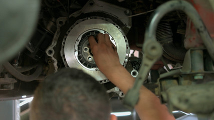 Auto mechanic is installing bolts into metal car clutch. Close up repairman inserting bolts into round car detail.