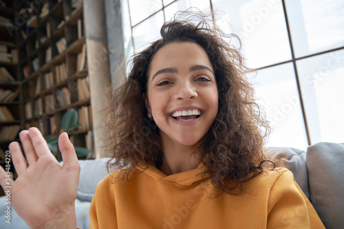 Fotografía Happy hispanic latin gen z teen girl blogger smiling face waving hand talking to webcam recording vlog, social media influencer streaming, making video call at home