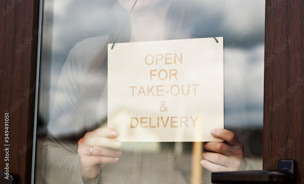 Woman holds the wooden sign with text: Open for take-out and delivery - obrazy, fototapety, plakaty 