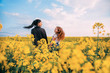 © kharchenkoirina - Family photography, mother and daughter look each other love. Happy two together. Long black hair brunette woman fly in wind. Redhead girl enjoy beauty blooming field blue sky. Yellow rapeseed flowers