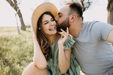 Close-up portrait of man hugging and kissing a woman on her cheek on a sunny day in a park, outdoors.