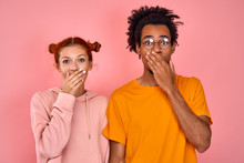 Embarrassed Young Mixed Race Couple Of Pretty Ginger Girl And Dark Skinned Guy Shyly Shut Their Mouths With Their Hands, Surprised By Some Startling Event. Concept Of Personal Life Among Young People