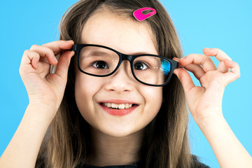 Poster - Close up portrait of a funny child school girl wearing looking glasses isolated on blue background.