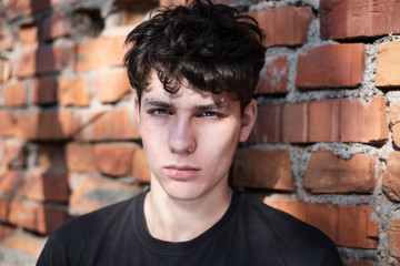 Handsome teenager on the background of an old brick house, the guy is sad because he is in a bad mood and has a headache