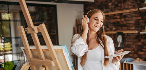 Fotografía Smiling young lady listening to music and painting picture, enjoying art therapy