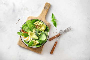 Canvas Print - Avocado salad with boiled eggs, broccoli, spinach and almond nuts in plate on white background. Top view.