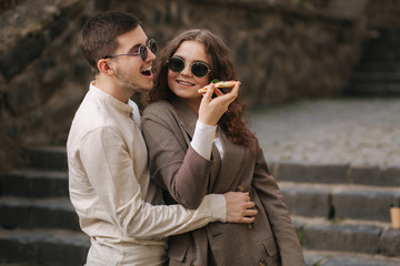 Smiling couple eating pizza outdoors. Man hol pizza box and take slice of vegan pizza. Stylish couple takeway pizza