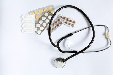 Wall Mural - Medical supplies on a white background top view. stethoscope, multi-colored tablets and vitamins in plates