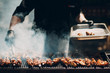  Man cooks shish kebab. Meat barbecue skewer and smoke in sunlight. Catering outdoor picnic.