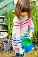 A Young Girl Watering Plants And Working In Her Home Garden.