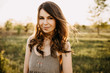 © Bostan Natalia - Close-up portrait of a young brunette woman with long wavy hair, standing in a field, outdoors, smiling, on summer day.